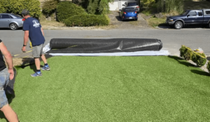 Workers laying down artificial grass in a residential yard, ensuring a smooth and professional installation. Transform your outdoor space with a flawless artificial grass installation.