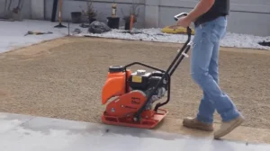 A worker using a compactor to prepare the ground for synthetic turf installation. Ensure a flawless turf installation with expert groundwork today!